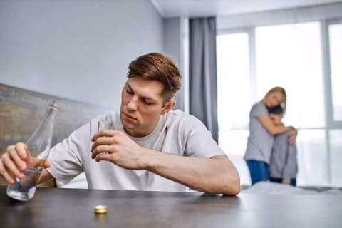 Man at a table while his wife and son looking scared in the background.
