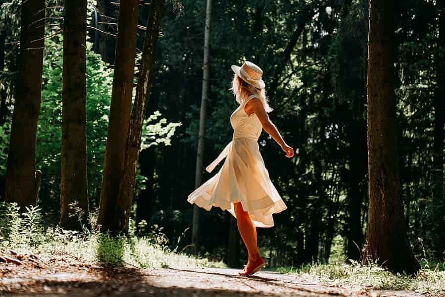 A woman is in a sun dress standing on her toes on a path in the woods.