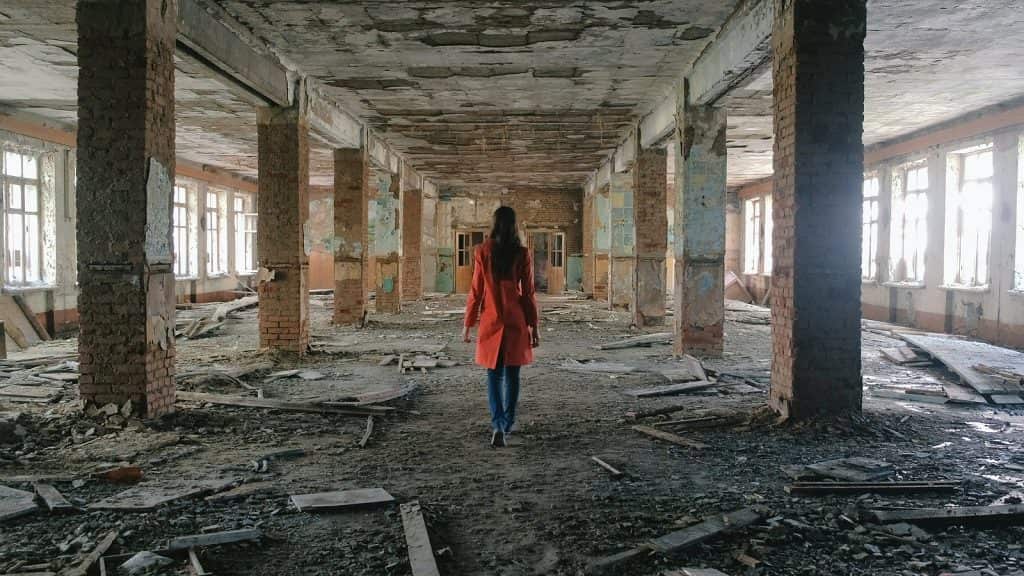 Woman walking through a damaged building symbolizing damage after betrayal.